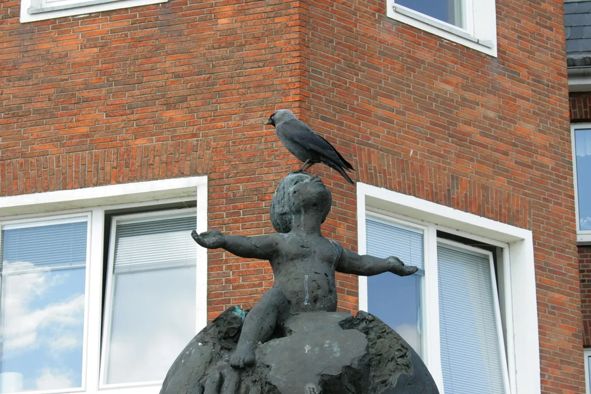 Rabenvogel auf einer Figur an einer Hausfassade, unmittelbar neben den Fenstern
