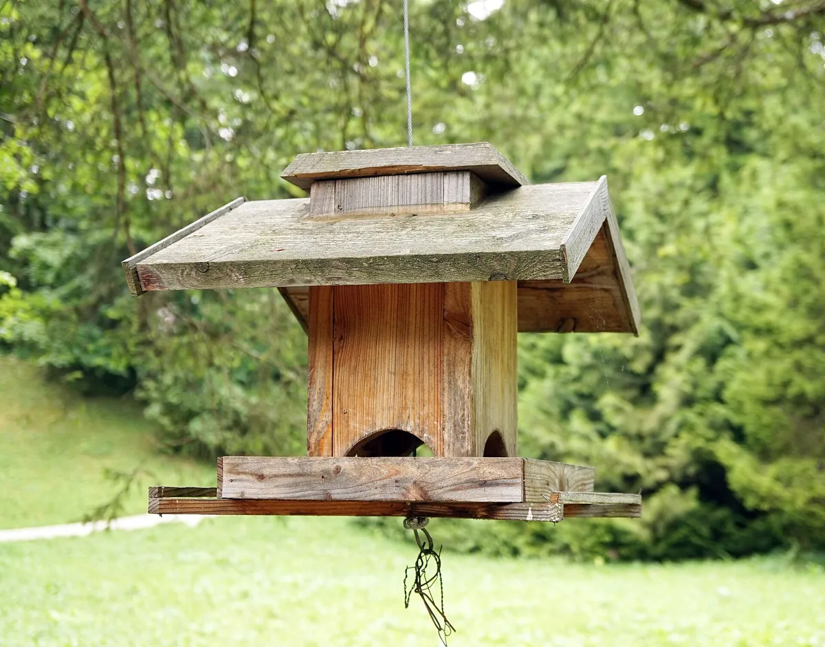 Hölzernes Vogelfutterhaus auf einem Ständer in einem Garten