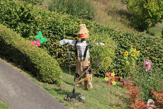 Vogelscheuche mit Hut am Rand eines bepflanzten Gartens